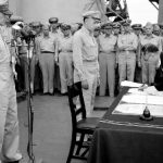 General Douglas MacArthur watches as the foreign minister Manoru Shigemitsu of Japan signs the surrender document ending WW2